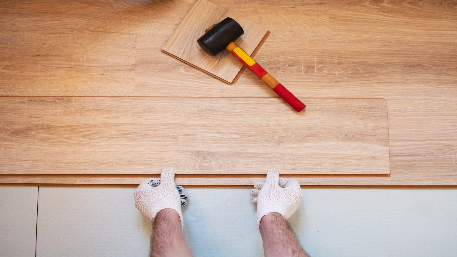 Hands with a hammer installing tiles on a floor as Basement Flooring Options