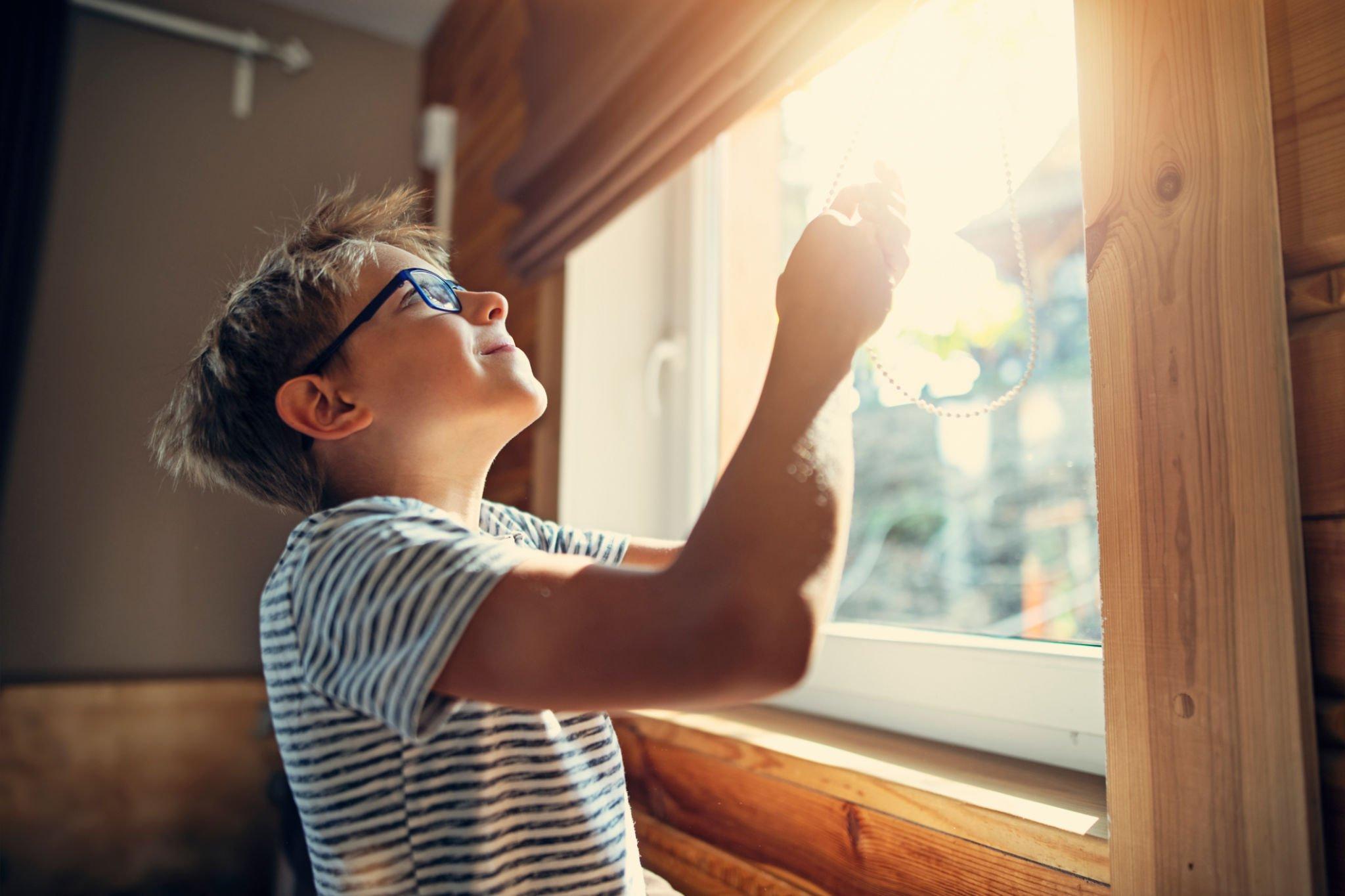 A boy blocking the natural light through basement window blinds